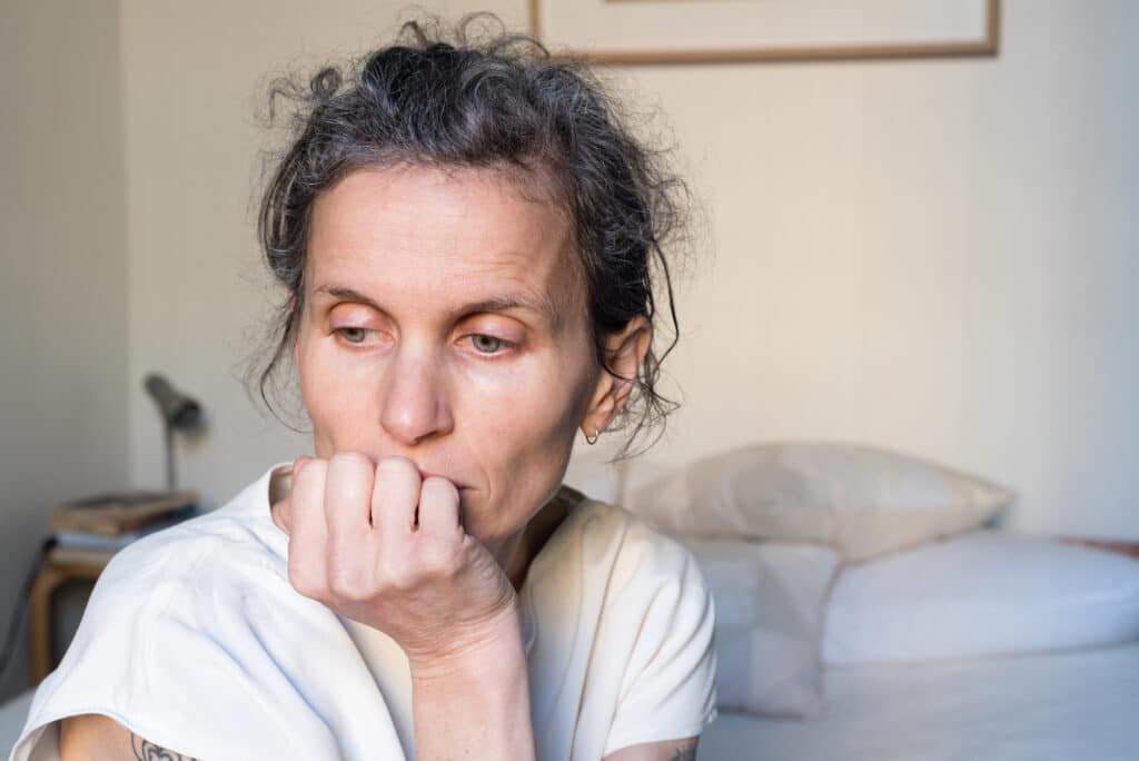 Close up of middle aged woman resting head on chin in bedroom (selective focus)